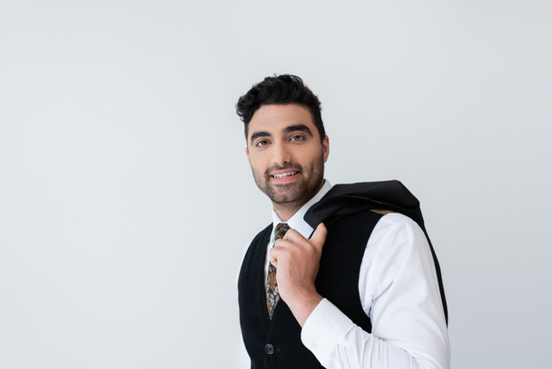 happy muslim man in vest holding blazer isolated on grey - Zdjęcie, obraz