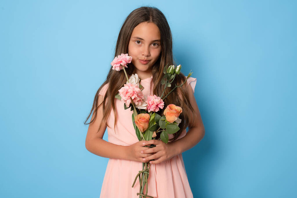 Portrait of attractive cheerful minded dreamy girl holding flowers copy space deciding isolated over blue background - Foto, afbeelding