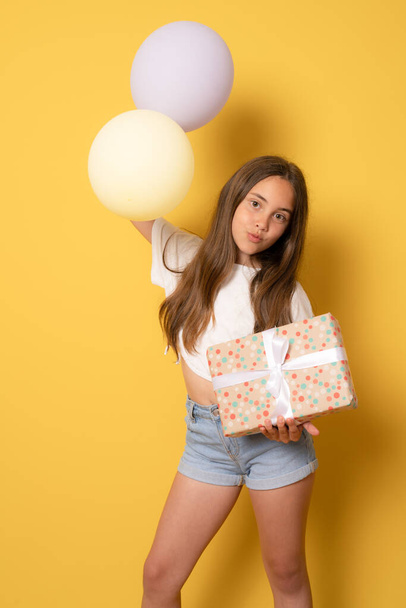 Młoda nastolatka dziewczyna trzyma balony i pudełko na izolowane żółte tło. - Zdjęcie, obraz