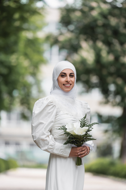 novia musulmana sonriente con anillo de diamante en el dedo celebración de ramo de boda  - Foto, Imagen