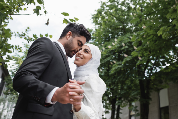 low angle view of happy muslim newlyweds with closed eyes holding hands - Photo, image