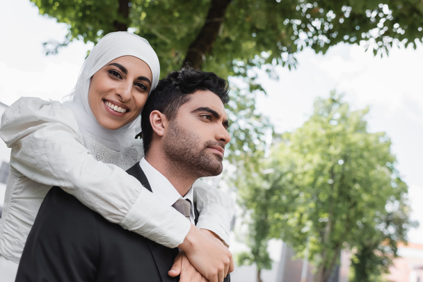 ευχαριστημένη νύφη με χιτζάμπ αγκαλιάζει μουσουλμάνο γαμπρό με κοστούμι  - Φωτογραφία, εικόνα