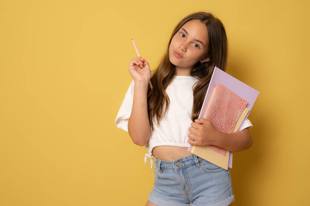 Mädchen geht isoliert auf gelbem Hintergrund zur Schule, sie hält Bücher und Notizbücher in den Händen, blickt in die Kamera - Foto, Bild