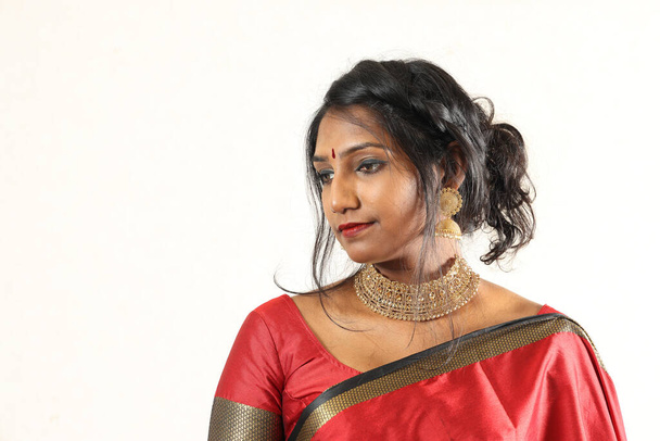 Indian woman wearing red orange traditional royal saree jewellery choker set necklace jhumka earring maang tikka waist chain stand pose look see smile mood expression at old rustic room background - Photo, Image