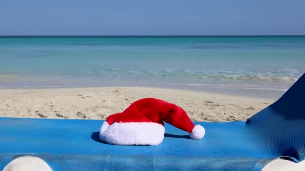 Images de la belle plage de Cuba Varadero, montrant un chapeau rouge de Noël placé sur le côté d'une chaise longue bleue, Noël au soleil et concept de plage, filmé en qualité 8K - Séquence, vidéo