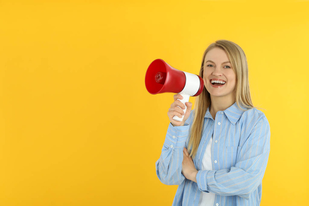 Young woman with megaphone on yellow background - Foto, imagen