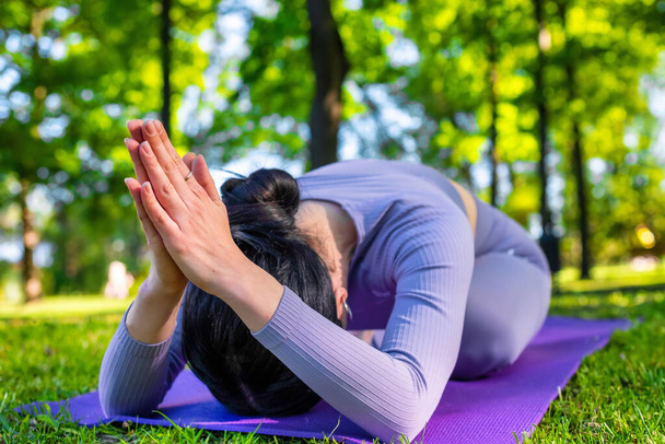 Chica atractiva con el pelo largo negro vestido de púrpura haciendo yoga plantea y meditando en el parque verde - Foto, imagen