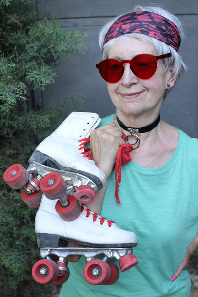 portrait en gros plan de femme mature avec des lunettes de soleil et des patins à roulettes vintage - Photo, image