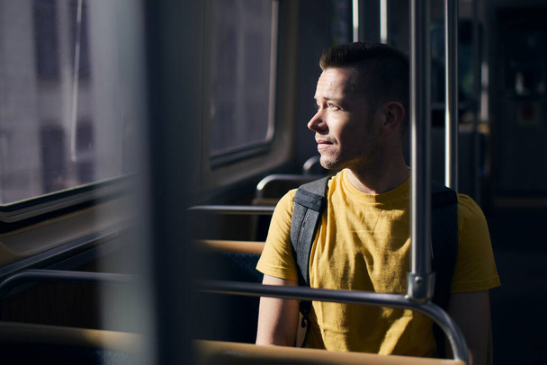 Pensive lonely man looking out of window of train. Solo traveler in public transportation on sunny day - Fotoğraf, Görsel