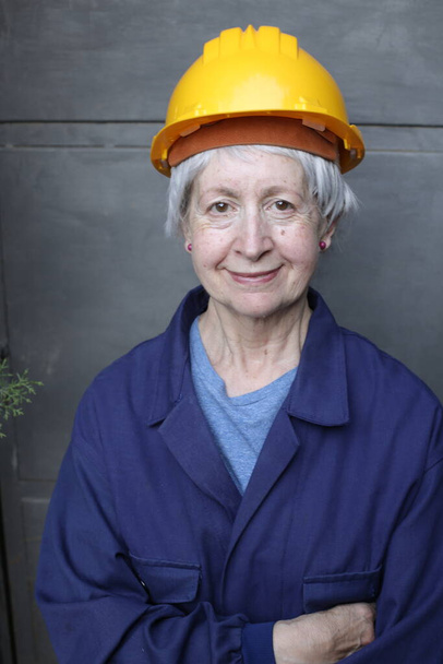 Nahaufnahme Porträt einer reifen Frau in Arbeiteruniform und Hut auf grauem Wandhintergrund - Foto, Bild