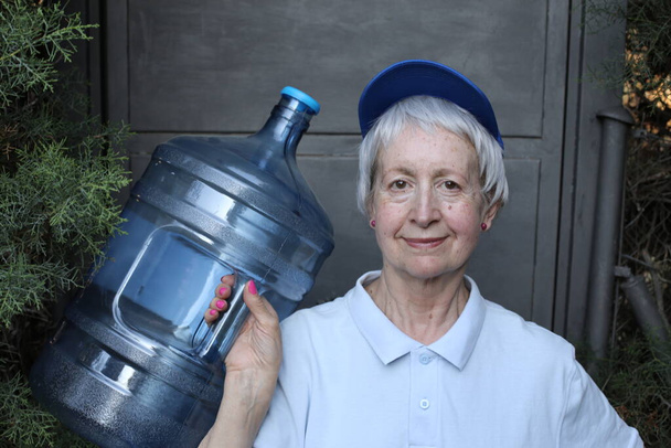 ritratto ravvicinato di donna matura dal servizio di consegna dell'acqua con grande bottiglia d'acqua - Foto, immagini