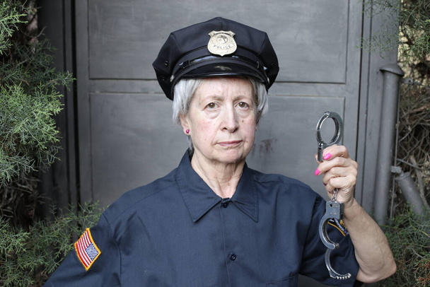 グレーウォールを背景に警察制服を着た熟女のクローズアップ肖像画 - 写真・画像