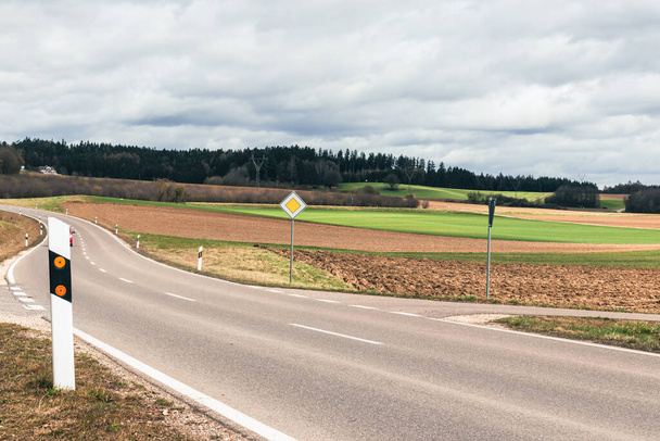Silniční značka hlavní silnice nastavena na silnici na pozadí zemědělských polí na jaře v zataženém počasí - Fotografie, Obrázek