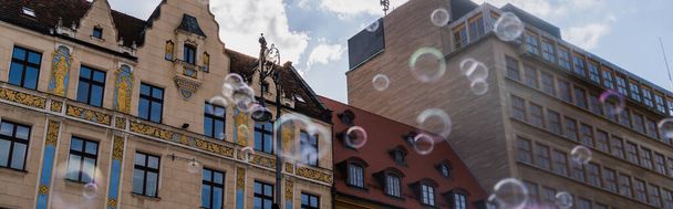 Low angle view of blurred soap bubbles near buildings on urban street in Wroclaw, banner  - Foto, Imagen