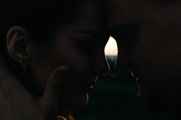 Sziluett egy férfiról és egy nőről, akik megérintik egymás homlokát naplementekor. - Fotó, kép