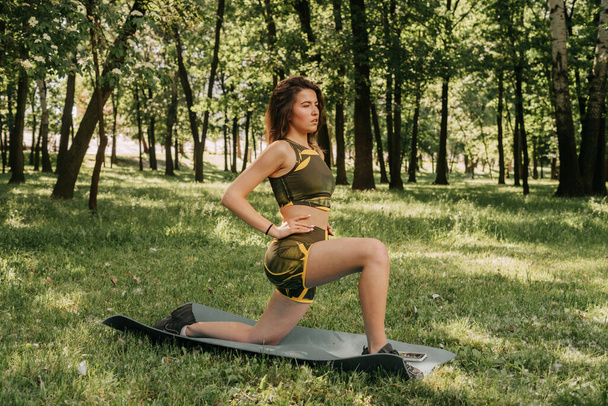 egy fiatal lány bemegy sportolni a parkba / az erdőbe. zöld ruhában egy jóga szőnyegen - Fotó, kép