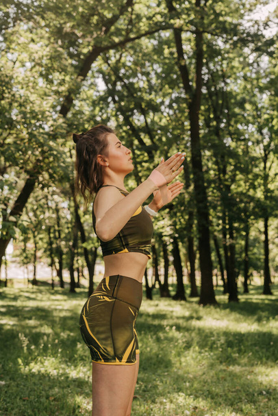 egy fiatal lány megy be sportolni rugalmas fitness a parkban / az erdőben. zöld ruhában egy jóga szőnyegen - Fotó, kép