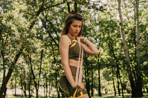 公園や森の中でフィットネス用の伸縮性のあるスポーツをする少女です。ヨガマットに緑のスーツを着て - 写真・画像
