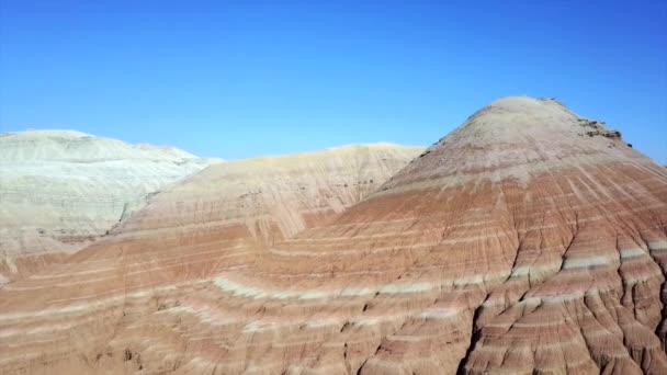 Gekleurde bergen van Aktau in de steppe. Kalkstenen bergen in het midden van de woestijn. Gekleurde heuvels van wit tot rood. Het aardegesteente wordt gescheiden door lagen. Een enorme kloof. Altyn Emel. - Video