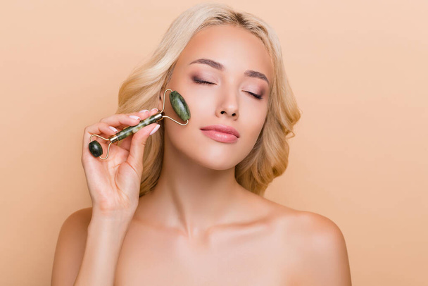 Portrait of adorable lady use nephrite gua sha to massage face anti age wrinkles correction isolated on beige color background. - Φωτογραφία, εικόνα