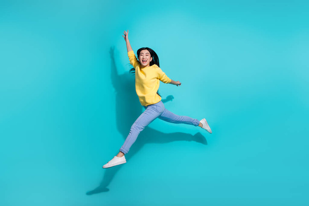 Full length photo of shiny excited woman wear yellow pullover dancing jumping high isolated teal color background. - Fotó, kép
