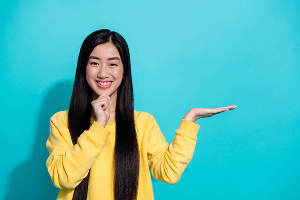 Photo of clever pretty woman wear yellow pullover arm chin holding arm empty space isolated teal color background. - Foto, Imagem