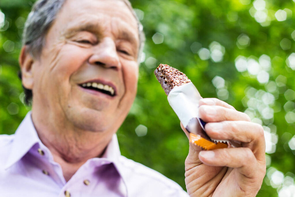 Älterer Mann isst einen Proteinriegel, gesunde Lebensstilkonzepte, Snack - Foto, Bild