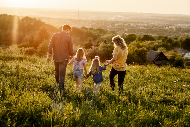 Vista trasera de la familia con dos hijas caminando en el prado  - Foto, Imagen