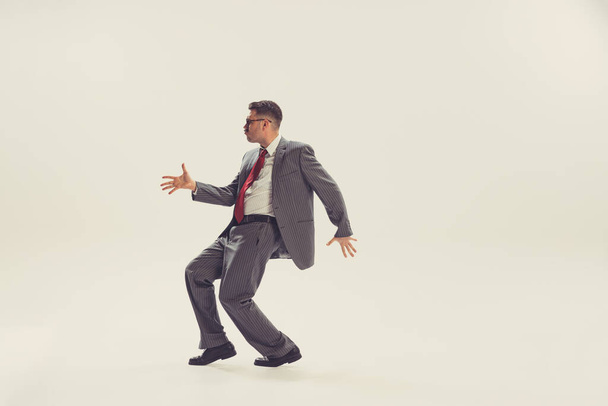 Fun. Portrait of young man, businessman dressed in suit in 50s, 60s fashion style dancing isolated on white background. Concept of modern culture, beauty and ad. Cyclical fashion. Copy space for ad - Fotó, kép