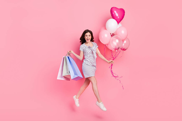 Photo of excited lady dressed dotted dress holding shoppers balloons jumping high isolated pink color background. - Фото, зображення