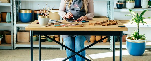 Anonimowa kobieta malująca gwiazdę zrobioną z gliny w swoim studio. Zrównoważony biznes: Nierozpoznawalna kobieta rzemieślnik robi ręcznie ceramiki ozdoby świąteczne, siedząc przy biurku warsztatowym z jej sprzętu. - Zdjęcie, obraz