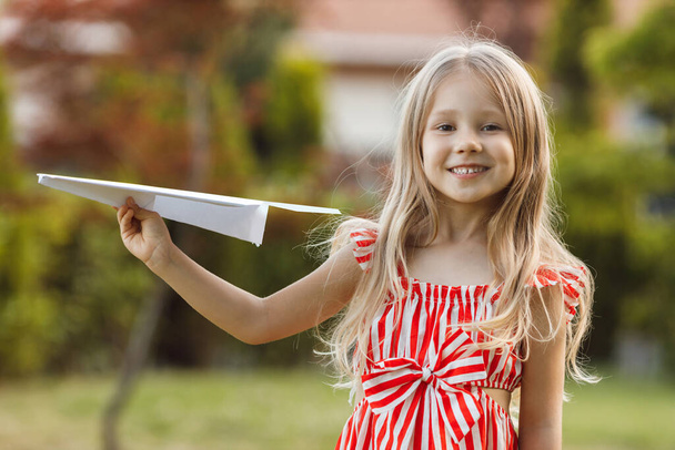 little cute girl with paper plane outdoor. High quality photo - Фото, изображение
