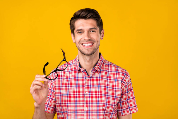 Portrait of attractive content cheerful guy holding in hand specs isolated over vibrant yellow color background. - Foto, Imagem