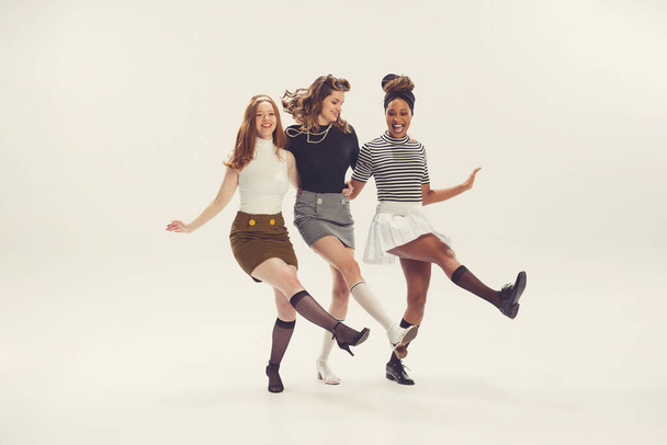 Dancing. Pretty young girls in retro 80s, 90s fashion style, outfits isolated over white studio background. Concept of eras comparison, beauty, fashion and youth. Look happy, excited, delighted - Foto, Imagen