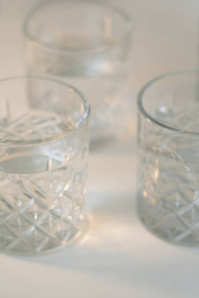 Vista de cerca de vasos facetados con agua limpia sobre fondo gris borroso - Foto, imagen