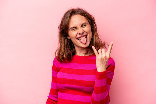 Young caucasian woman isolated on pink background showing rock gesture with fingers - Valokuva, kuva