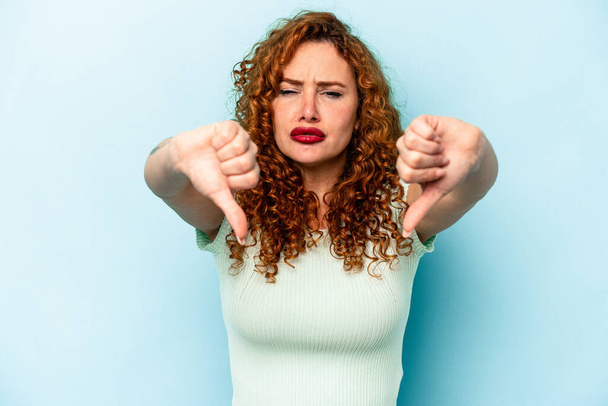 Young ginger caucasian woman isolated on blue background showing thumb down and expressing dislike. - Фото, зображення