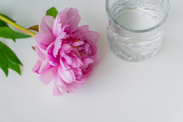 high angle view of fresh pink peony and faceted glass with pure water on white surface - Zdjęcie, obraz