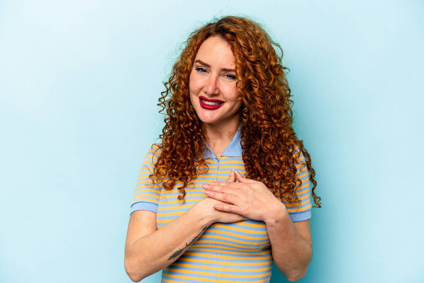 Young ginger caucasian woman isolated on blue background has friendly expression, pressing palm to chest. Love concept. - Photo, Image
