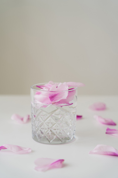 transparant glas met gin tonic en bloemblaadjes op wit oppervlak geïsoleerd op grijs - Foto, afbeelding