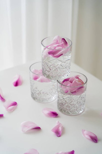 bicchieri di cristallo con petali tonici e floreali su tavolino bianco e fondo grigio - Foto, immagini