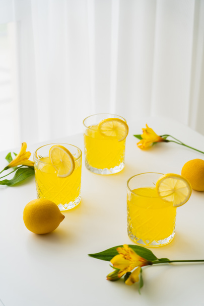 verres de limonade avec des tranches de citron juteux près des alstroemerias sur la table blanche - Photo, image