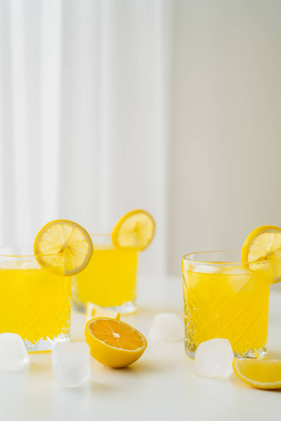 natural citrus tonic and sliced lemons near ice cubes on grey background - Zdjęcie, obraz