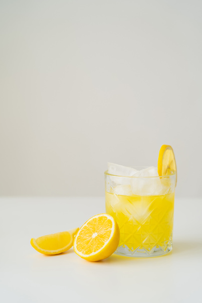 citrus tonic with ice cubes near cut lemon on white surface isolated on grey - Photo, Image