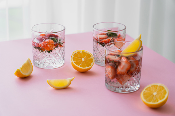 eau tonique fraîche avec des fraises hachées près de citrons coupés sur le dessus de table blanc - Photo, image