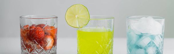 citrusový džus v blízkosti jahodové tonikum a sklo s ledem na šedém pozadí, banner - Fotografie, Obrázek