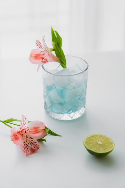 glass with iced tonic water near pink alstroemeria flowers and lime on white surface - Photo, Image