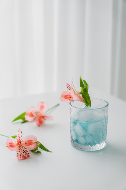glas met koude tonic en roze alstroemeria bloem op witte tafelblad en grijze achtergrond - Foto, afbeelding
