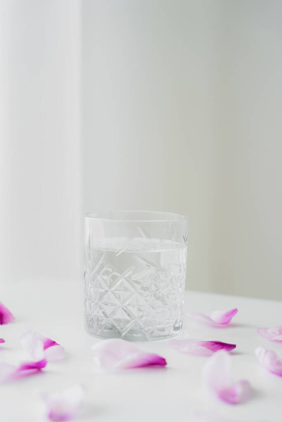 floral petals near glass with fresh water on grey background with copy space - Foto, Bild