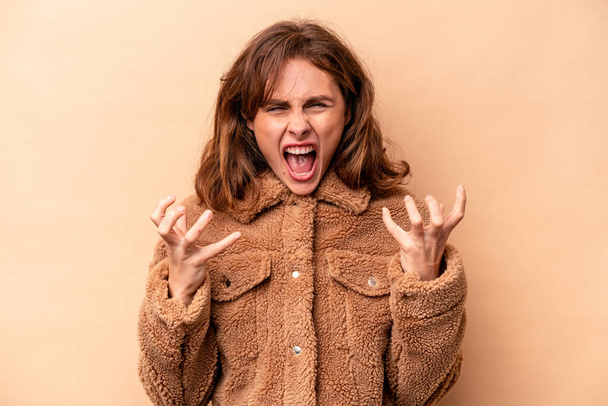 Young caucasian woman isolated on beige background screaming with rage. - Photo, Image